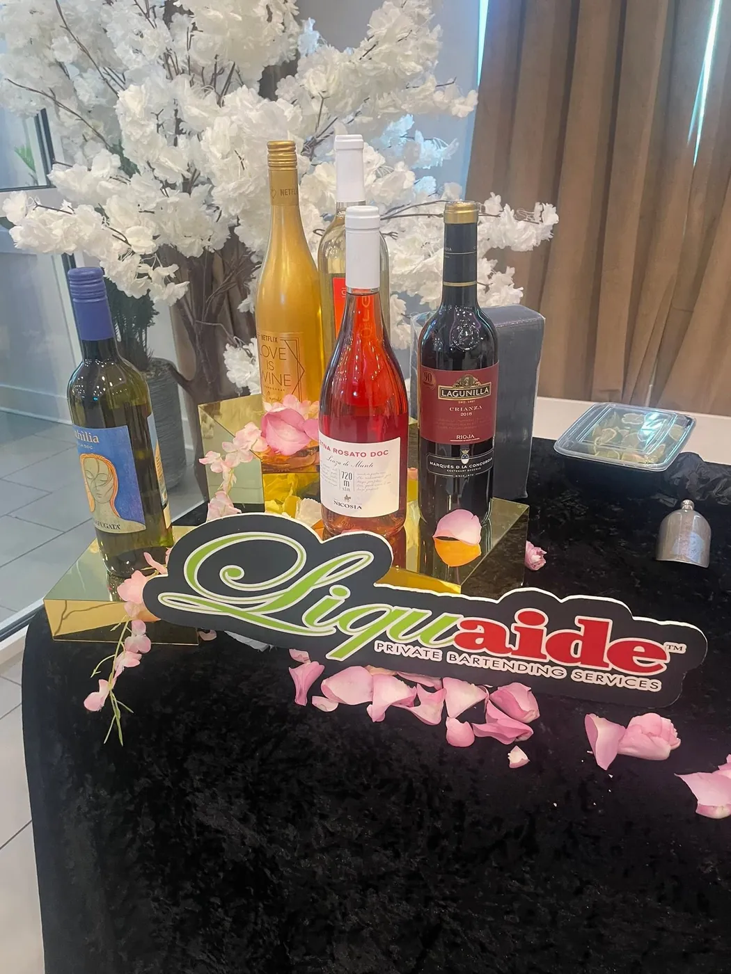 Elegant wine bottle centerpiece with rose petals and the Liquaide logo